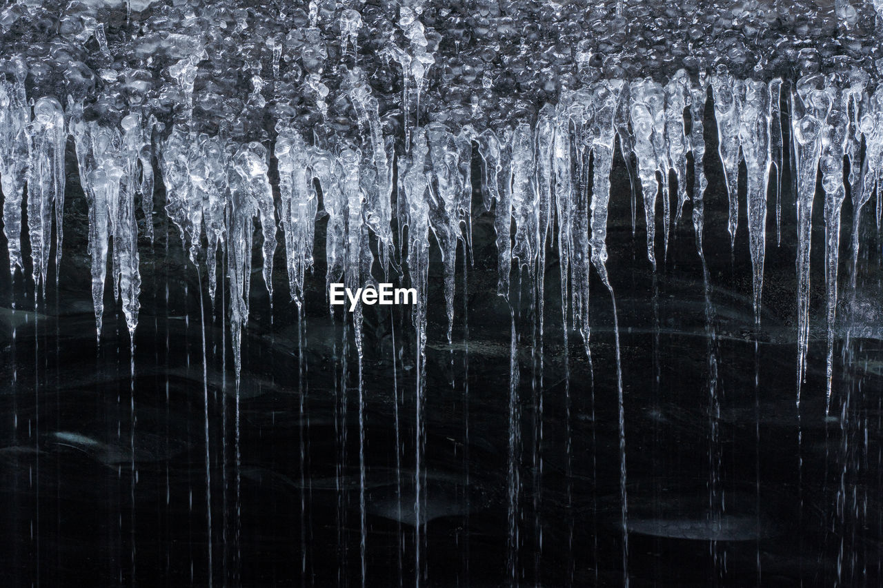 Clean water falling down from icicles inside dark icy cave in vatnajokull national park in iceland