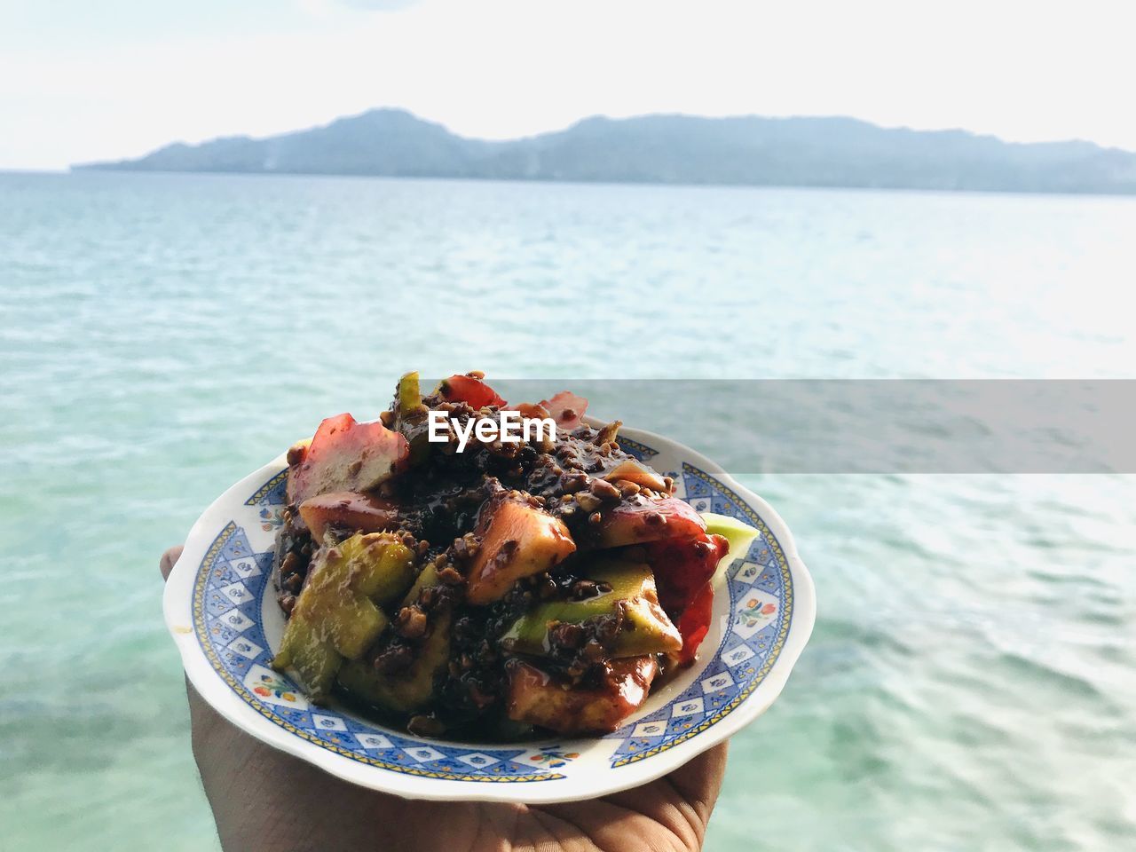 Close-up of hand holding food in sea against sky