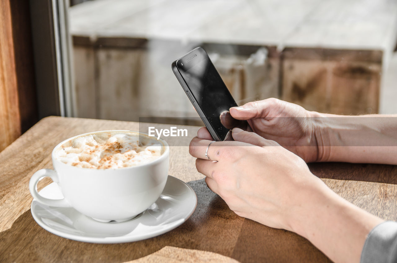 Cropped hand of businesswoman using mobile phone by coffee in cafe