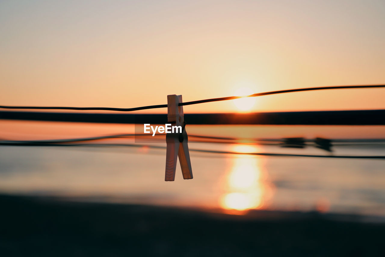 Close-up of clothespins on rope against sky during sunset