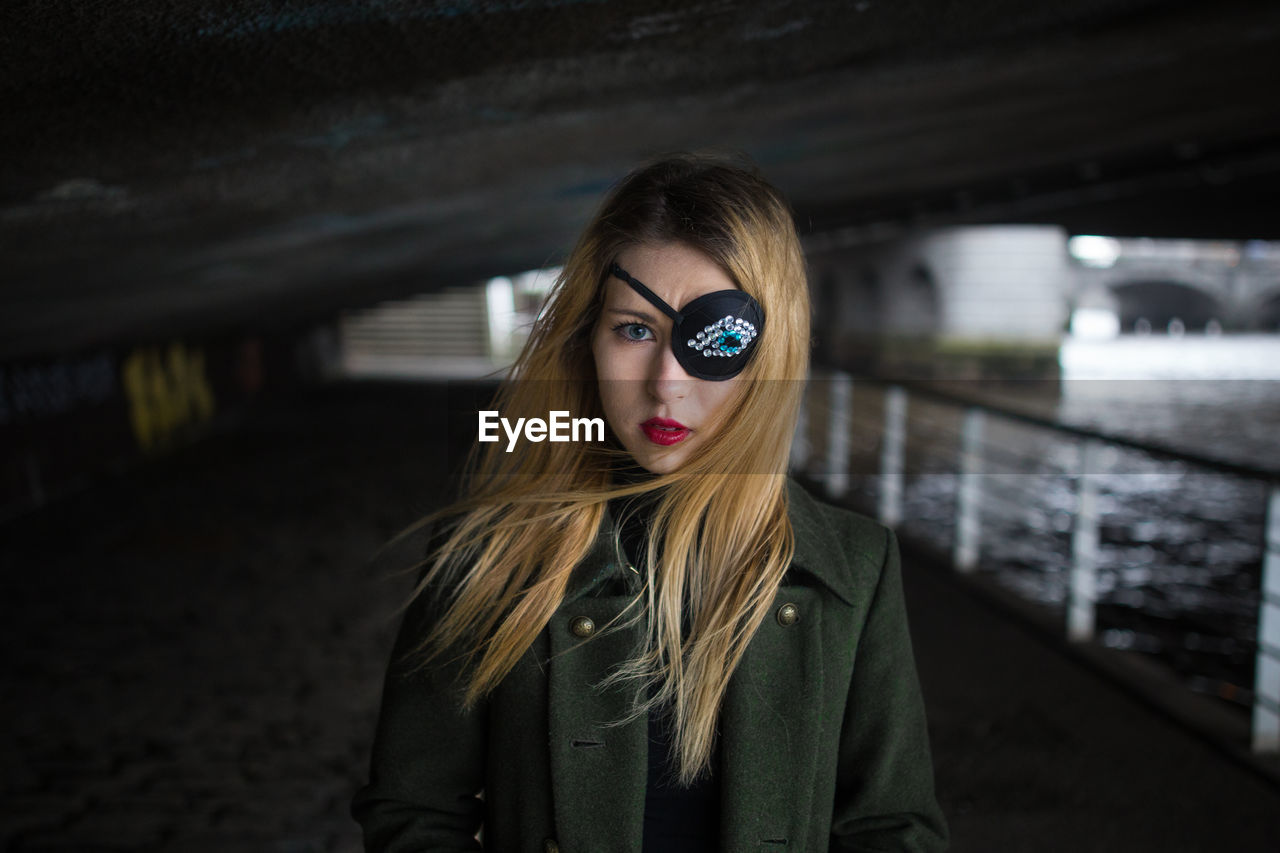 Portrait of young woman wearing costume eye patch below bridge