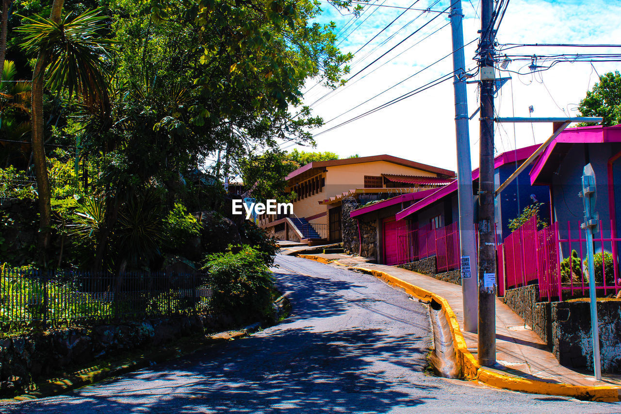 WALKWAY AMIDST BUILDINGS AND TREES AGAINST SKY