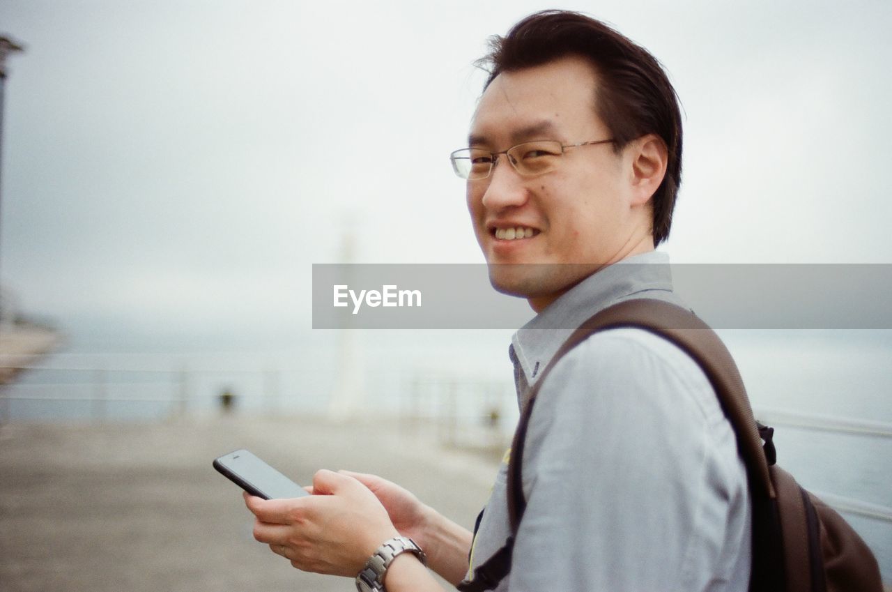 Portrait of smiling young man using mobile phone in city
