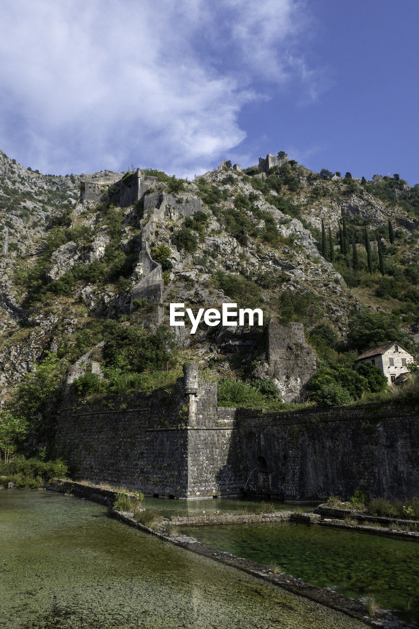 sky, plant, cloud, nature, mountain, rock, tree, travel destinations, architecture, land, environment, no people, scenics - nature, history, travel, ruins, landscape, the past, tourism, beauty in nature, outdoors, built structure, terrain, mountain range, non-urban scene, day, ancient, cliff, grass, old ruin, tranquility, water
