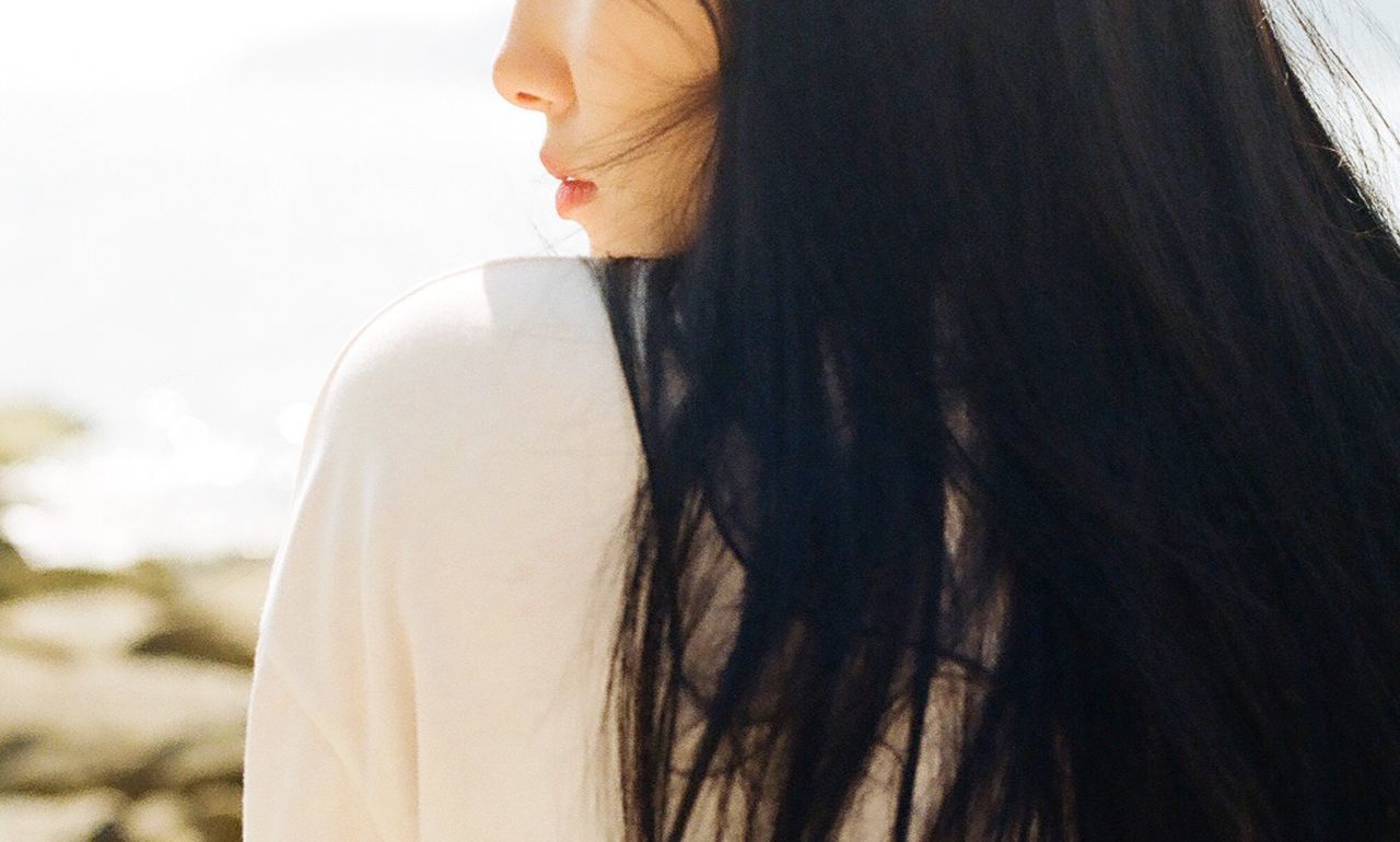 CLOSE-UP REAR VIEW OF YOUNG WOMAN STANDING AGAINST SKY