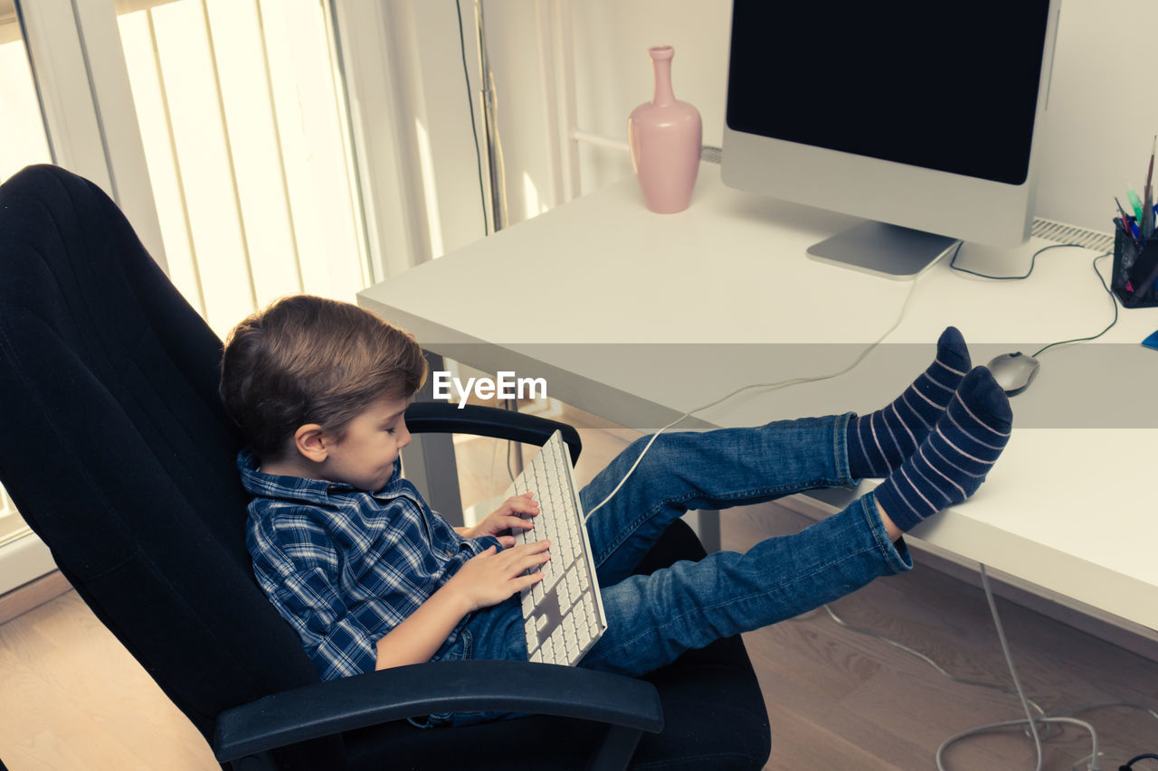 Little boy typing on computer keyboard while surfing the net on desktop pc.