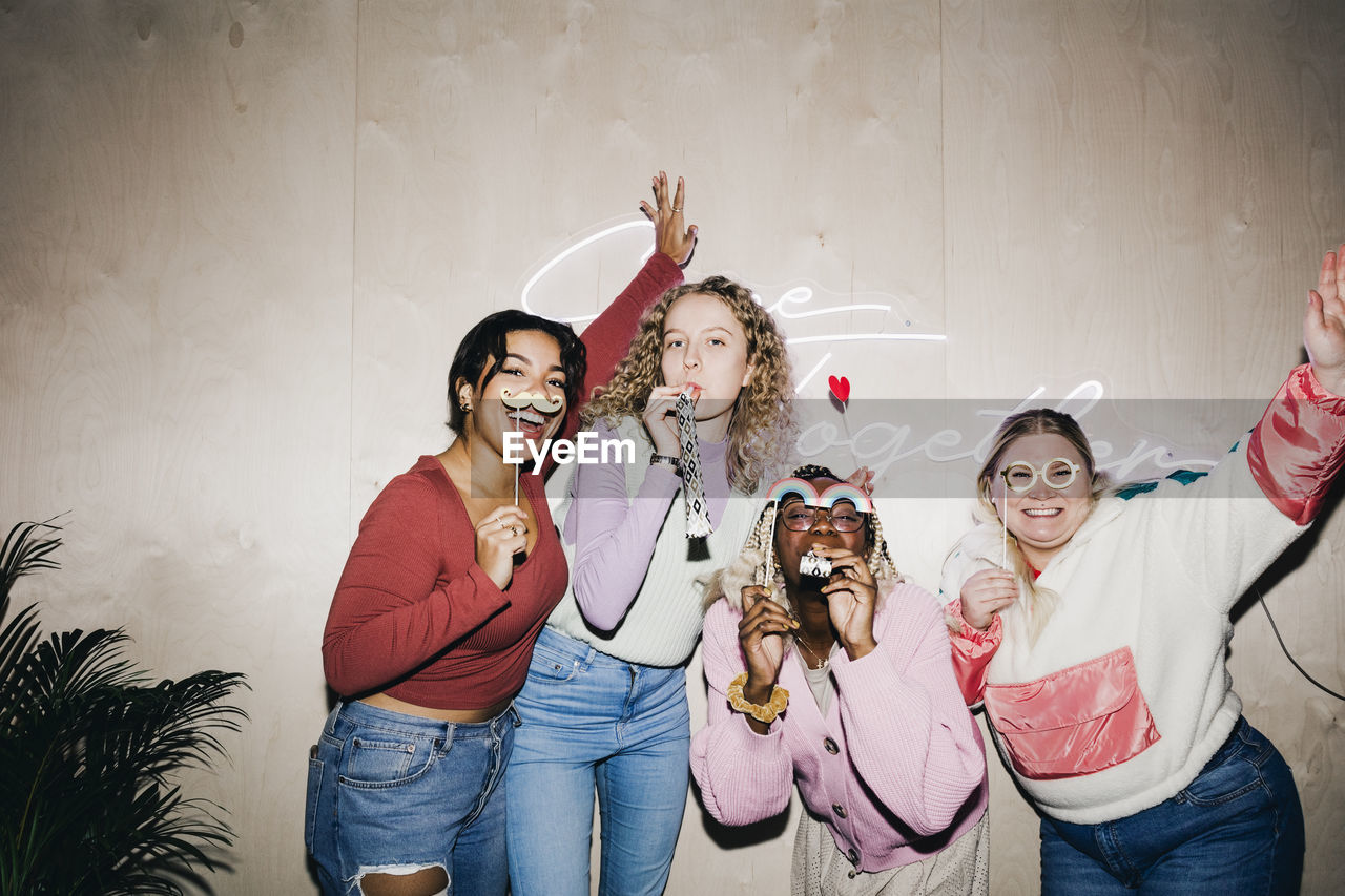 Portrait of happy multiracial female students with props against wall in college dorm