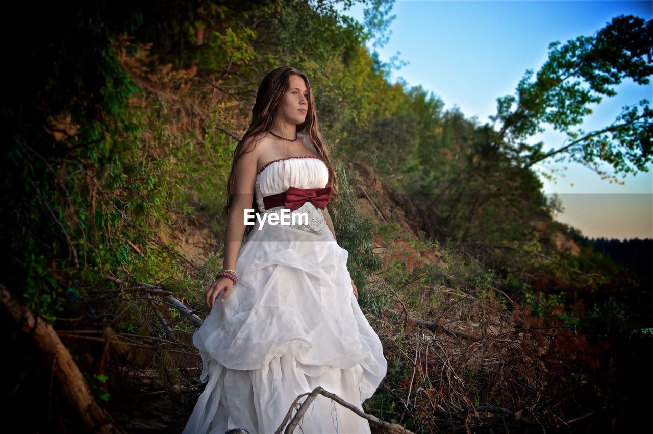 Young woman wearing white dress while standing in forest