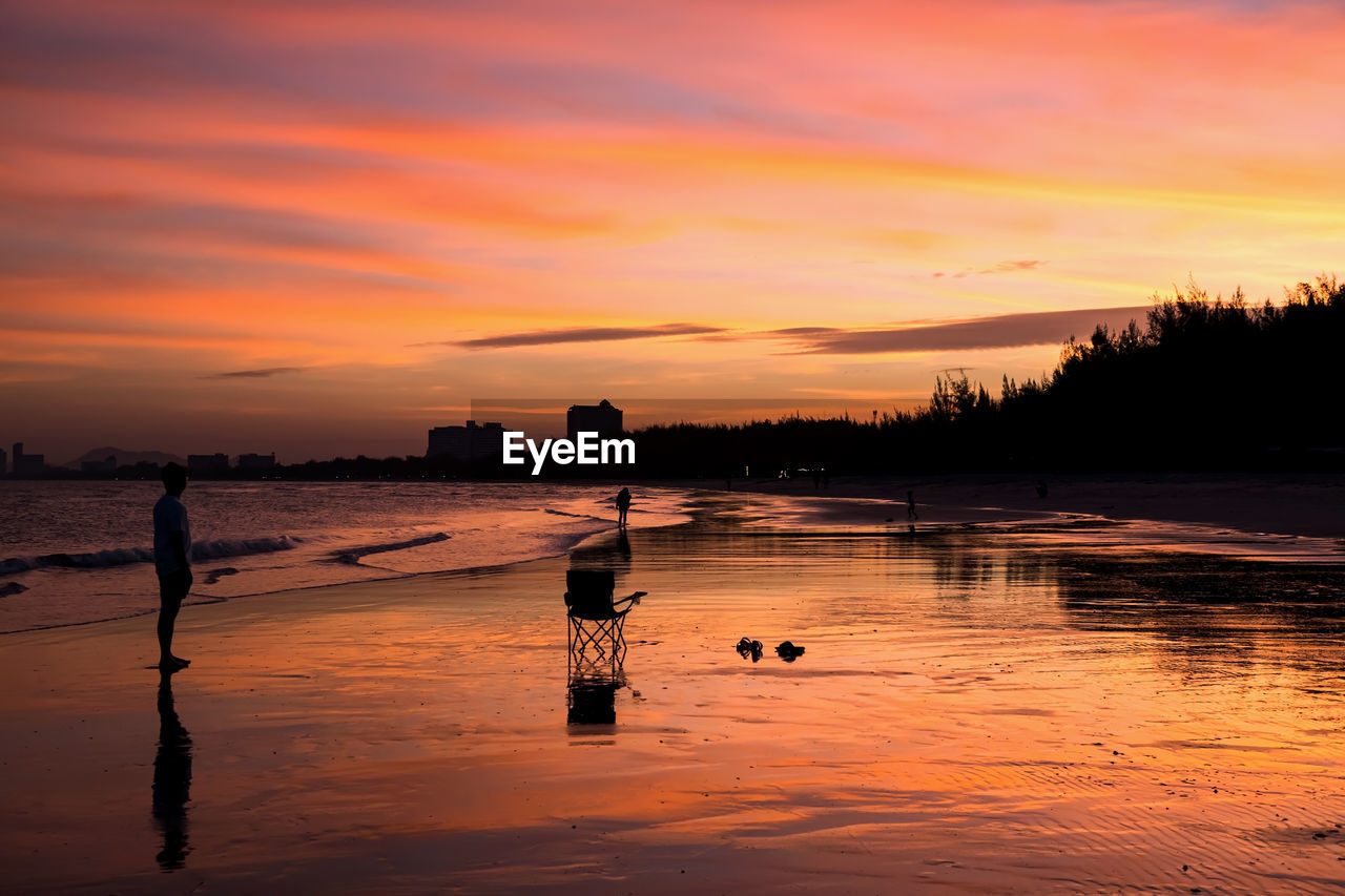 Silhouette man look at his happy family relax on beach with twilight sunset sky in cha-am