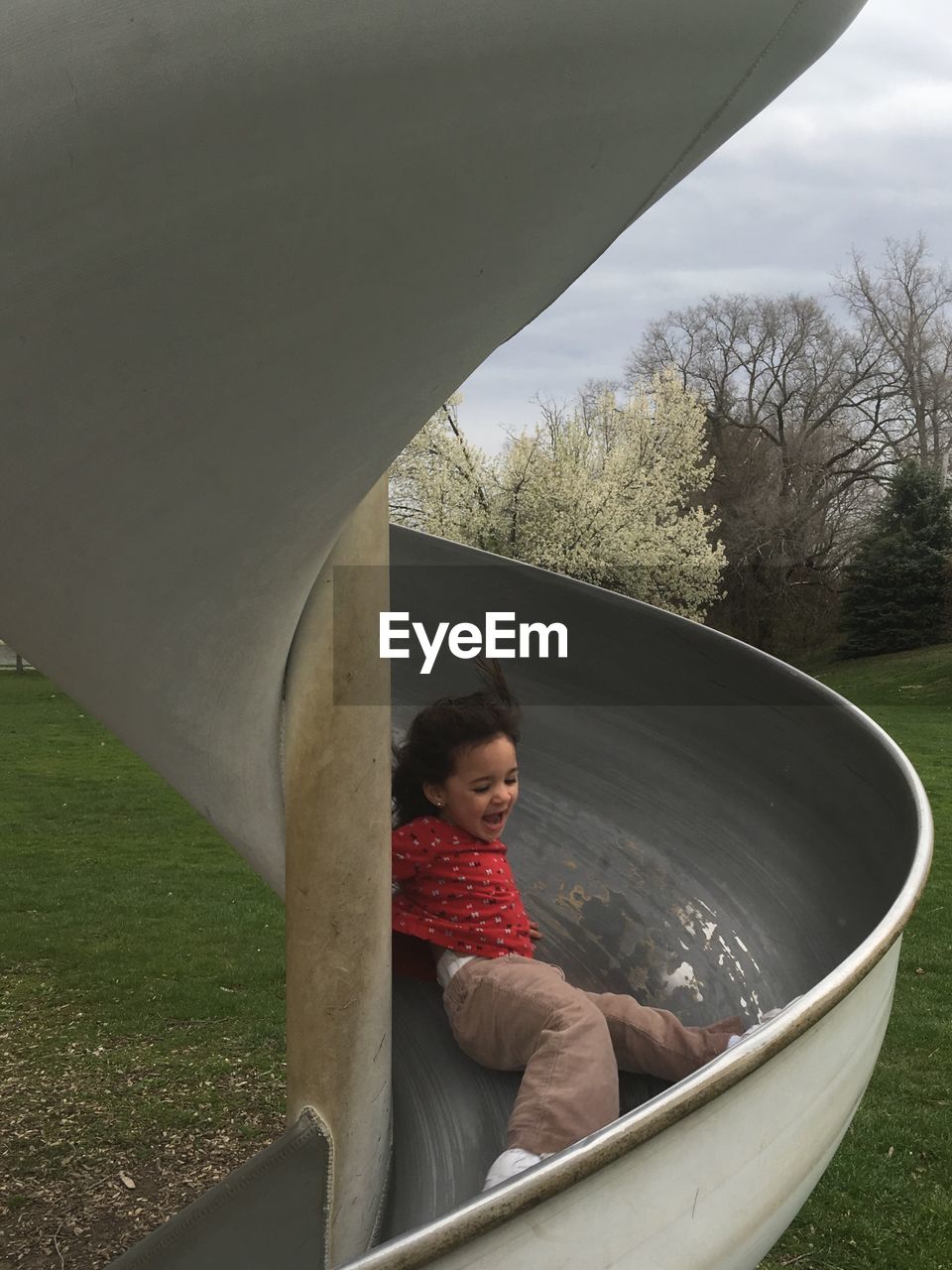 Low angle view of playful girl sliding in playground