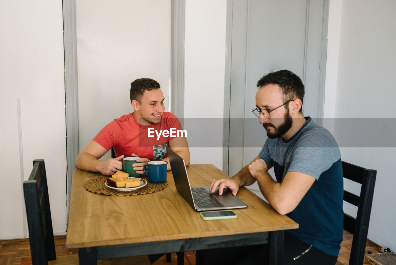 Two men sitting using laptop and phone.