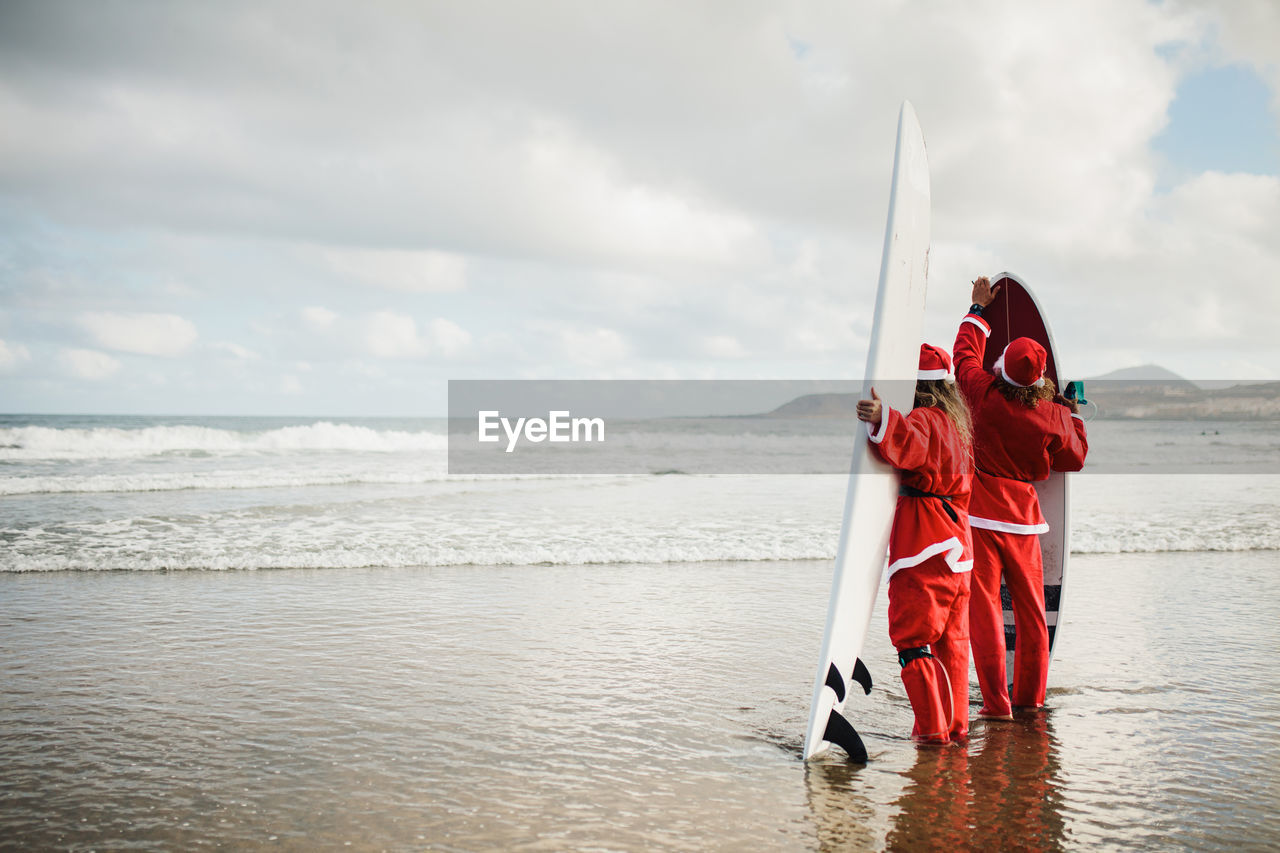 Couple wearing santa costumes holding surfboards in sea