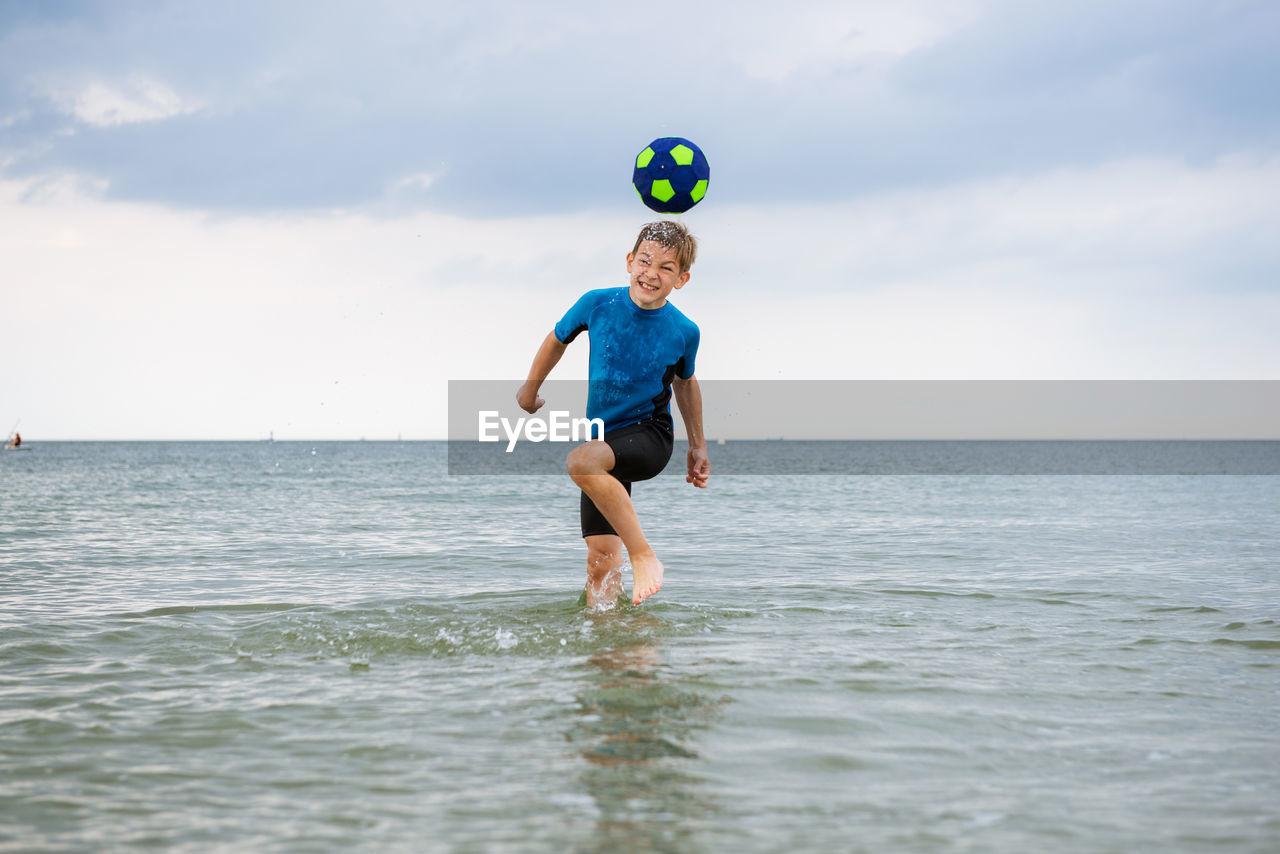 Cheerful boy playing with ball in sea