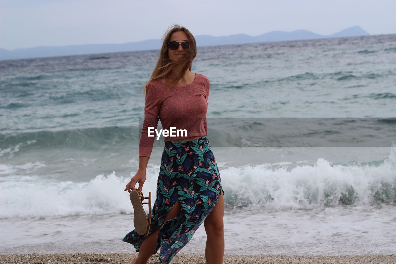 Young woman standing at beach against sea