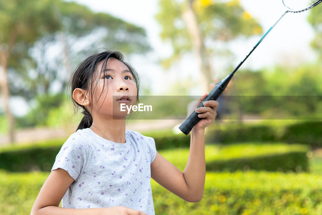 Girl holding badminton racket while standing by plants