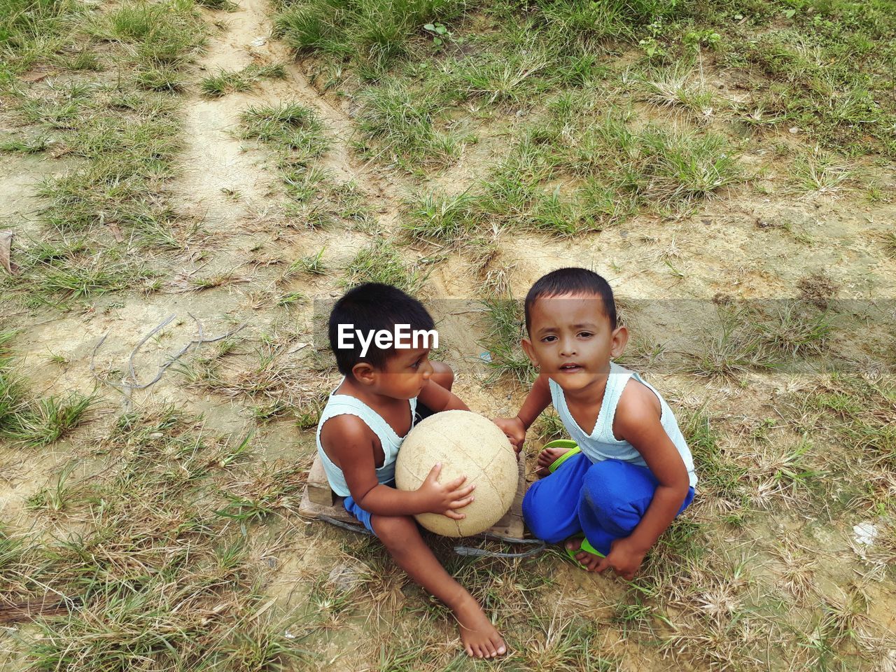 HIGH ANGLE VIEW OF SIBLINGS SITTING ON FIELD