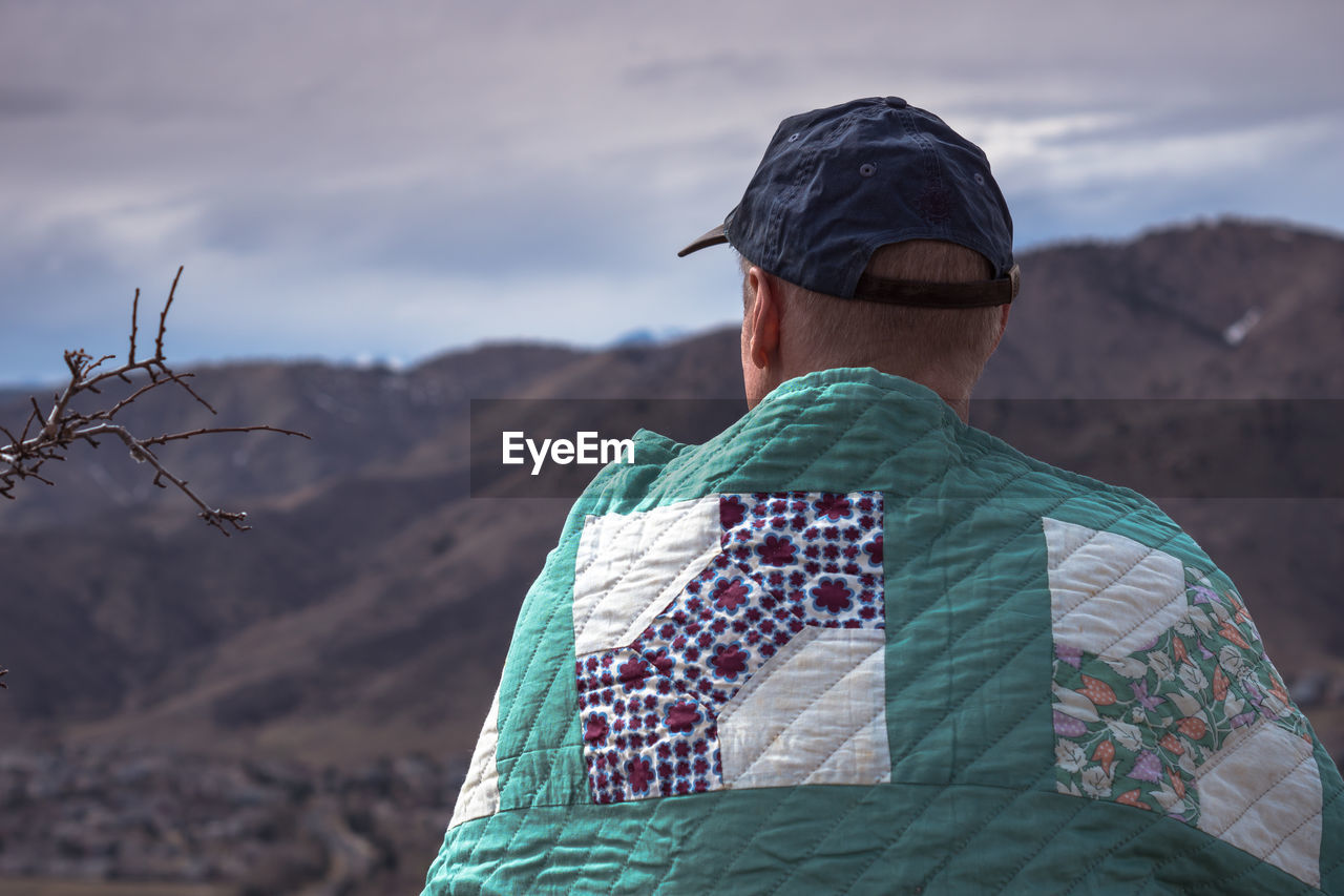 Rear view of man with blanket looking at mountains against sky