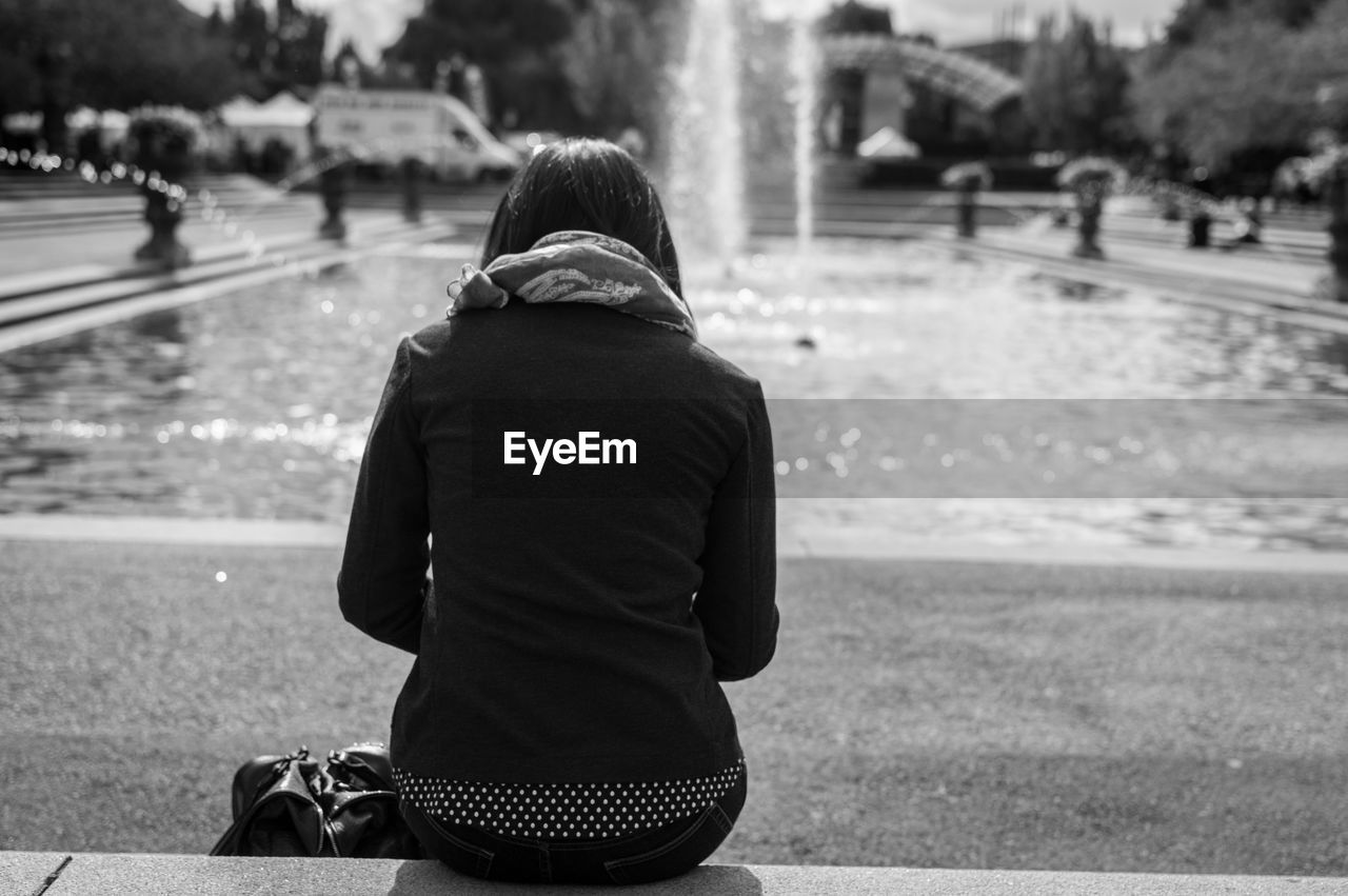 Rear view of woman sitting in front of fountain in park