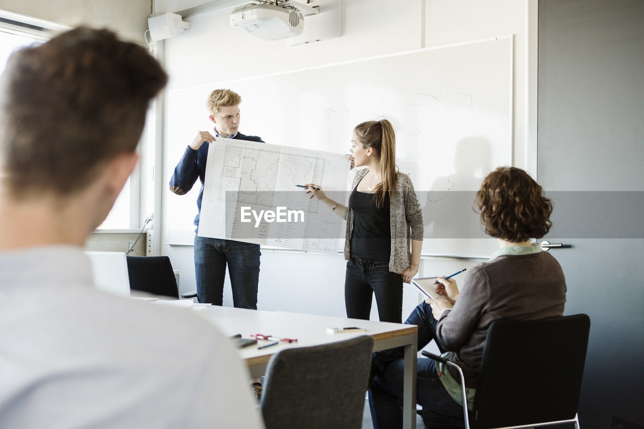 Young woman showing flipchart to friends and professor in classroom