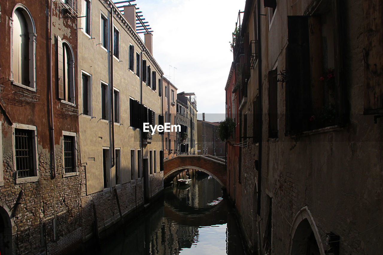 BRIDGE OVER CANAL AMIDST BUILDINGS AGAINST SKY