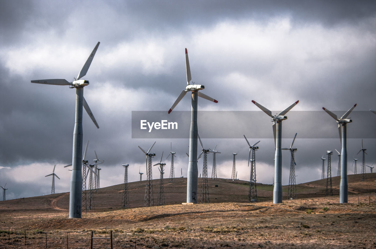 Windmills on field against cloudy sky