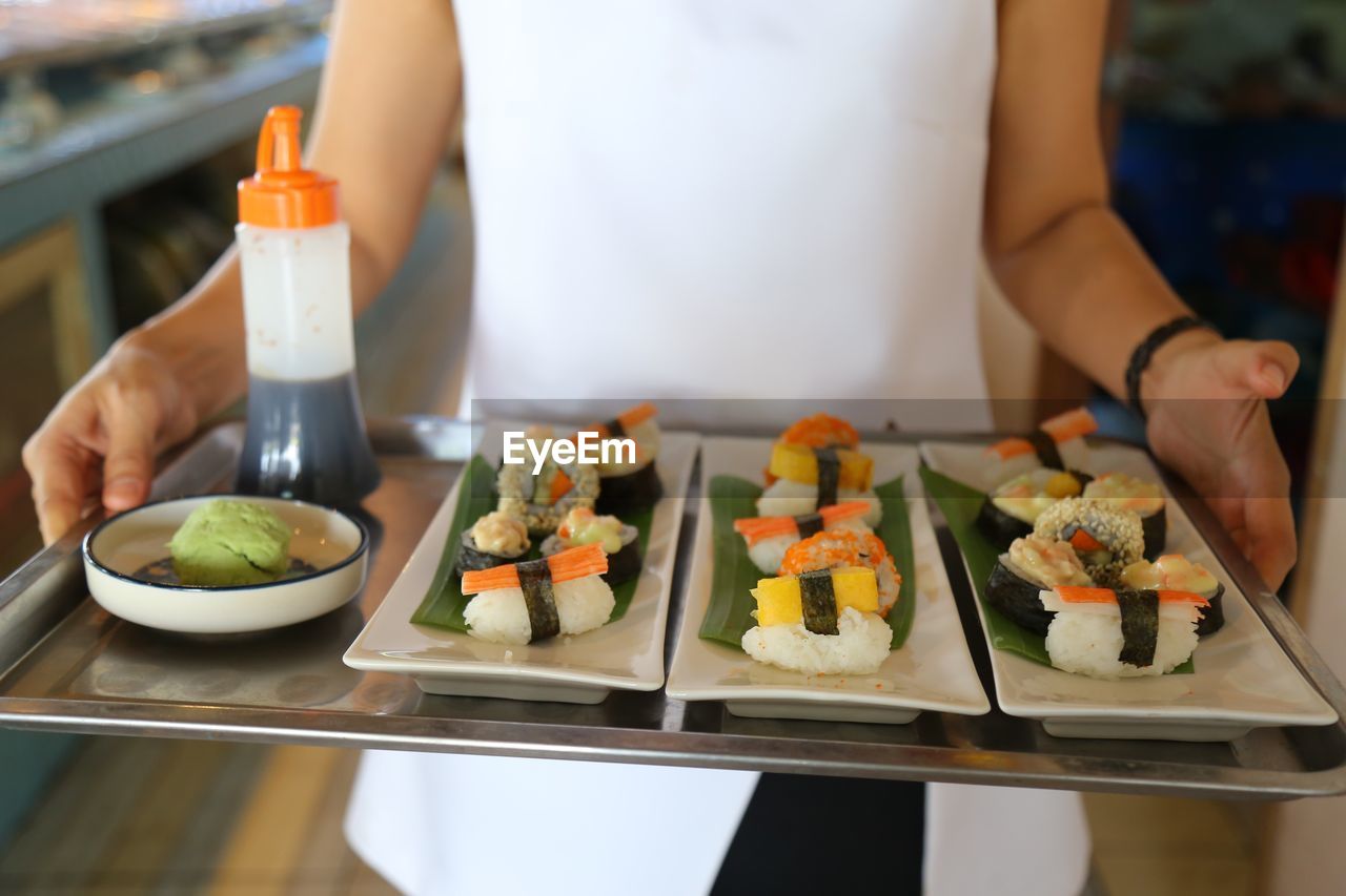 Midsection of waitress holding sushi in tray at restaurant