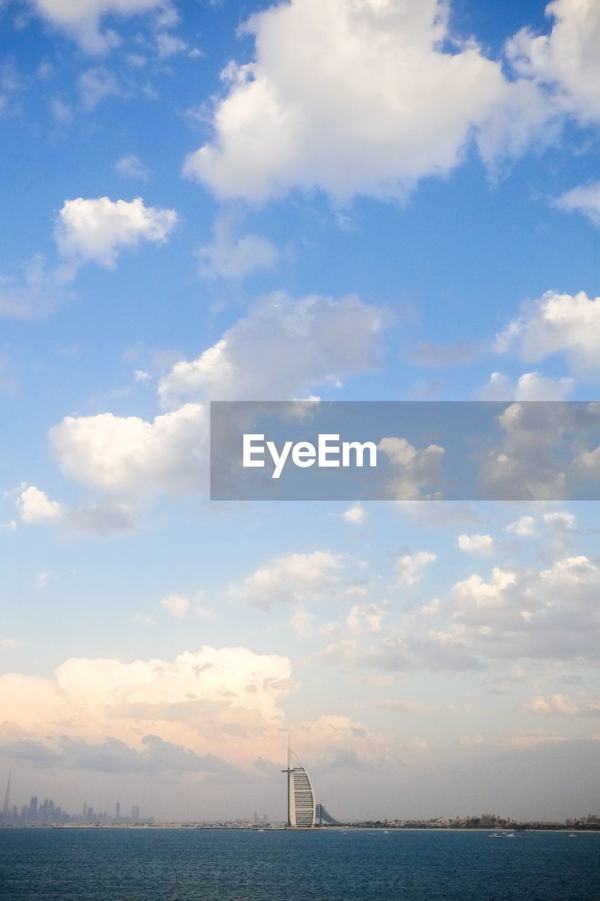 VIEW OF CITY AT WATERFRONT AGAINST CLOUDY SKY