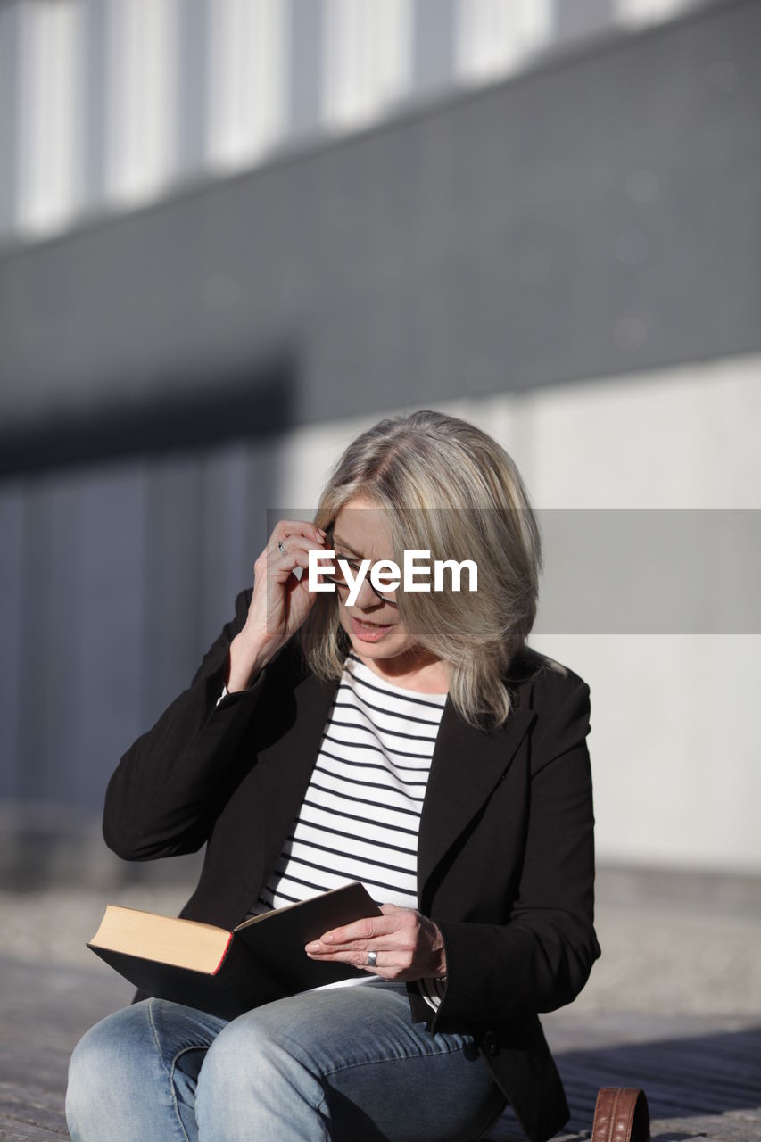 Mature businesswoman reading book sitting outdoors