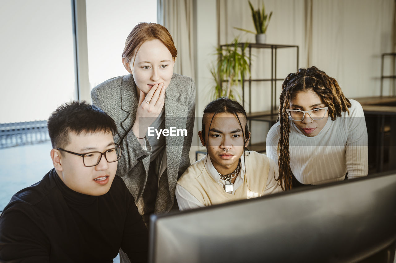 Multiracial programmers brainstorming over computer in creative office