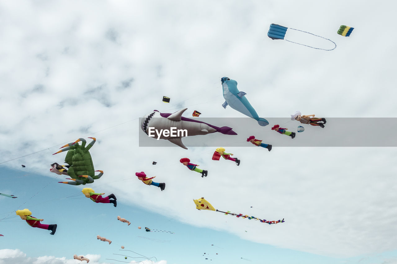 Low angle view of various colorful balloons flying against cloudy sky