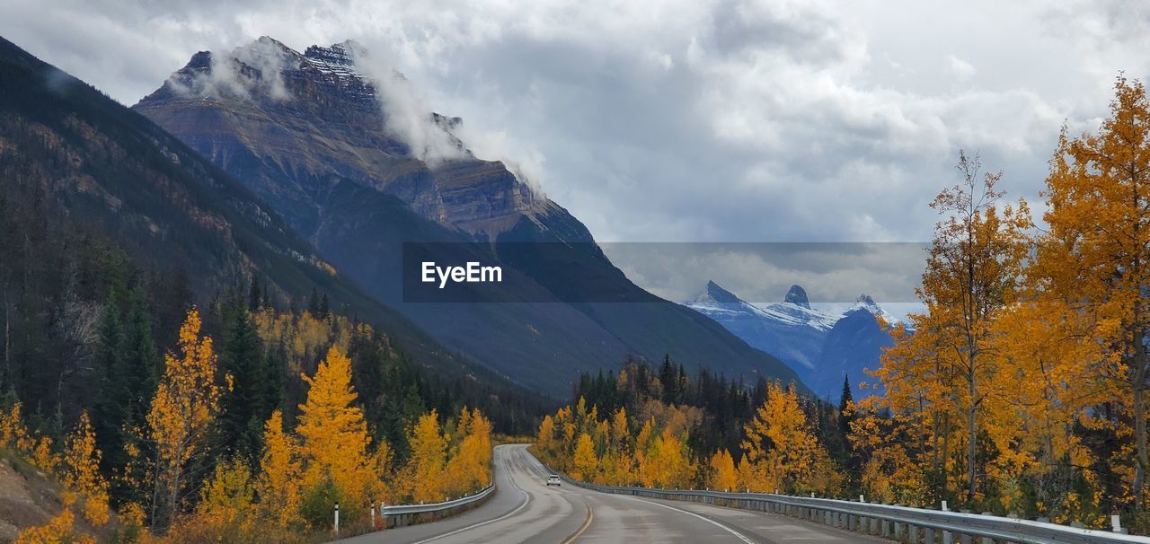 Road amidst trees and mountains against sky