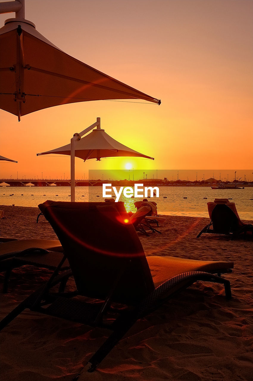 Lounge chair at beach against sky during sunset