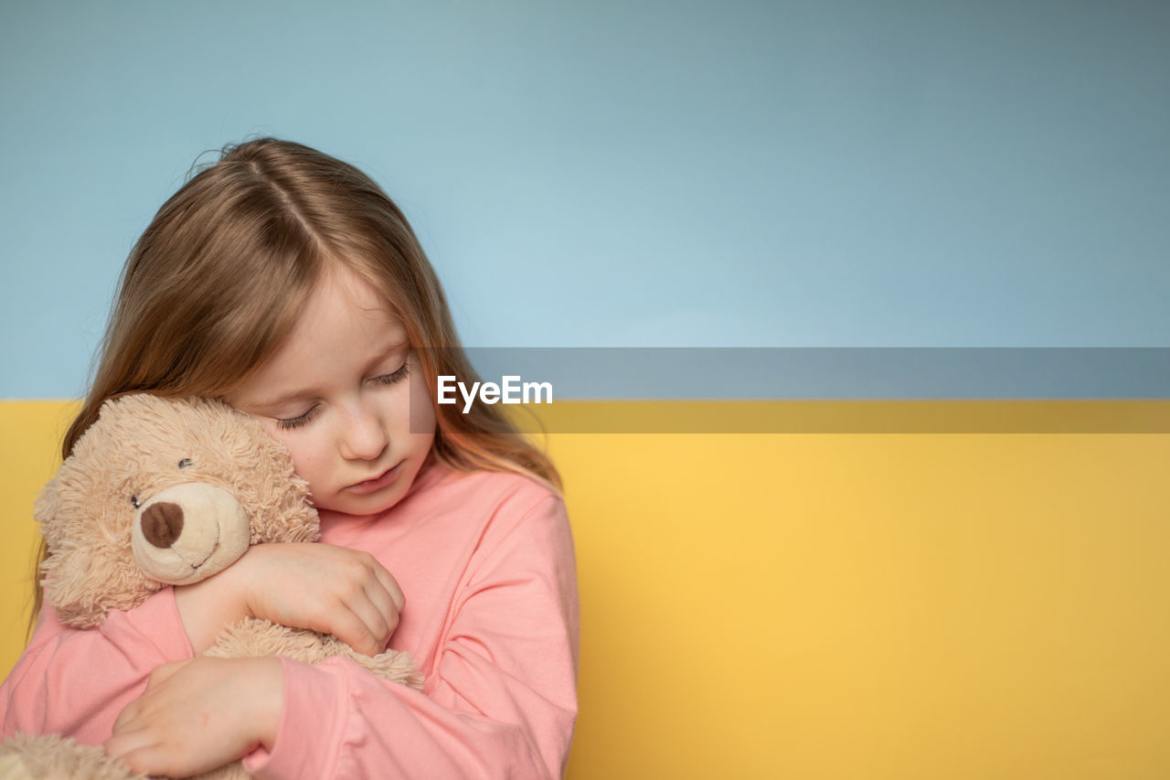 Cute girl embracing teddy bear against wall