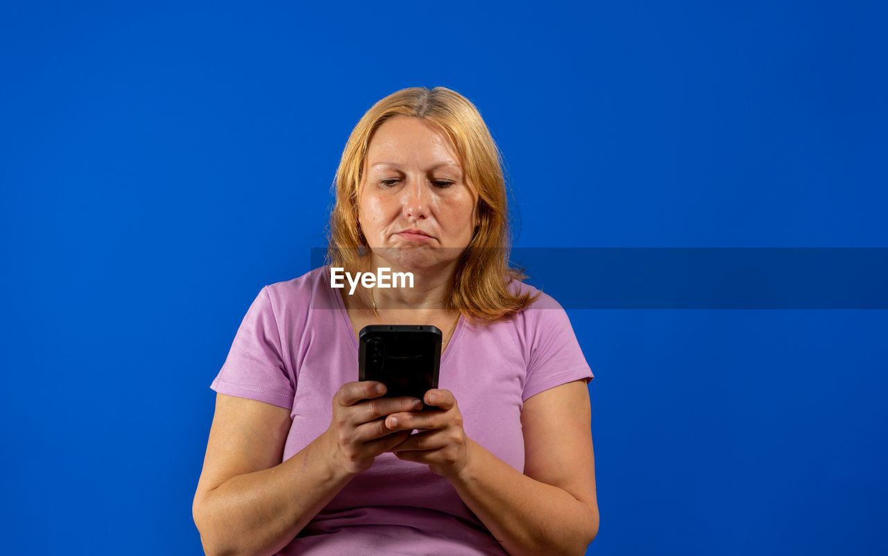 YOUNG WOMAN USING MOBILE PHONE AGAINST BLUE SKY