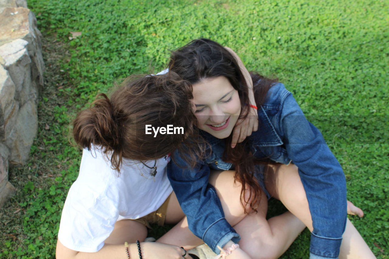 High angle view of woman kissing girlfriend while sitting on land in park