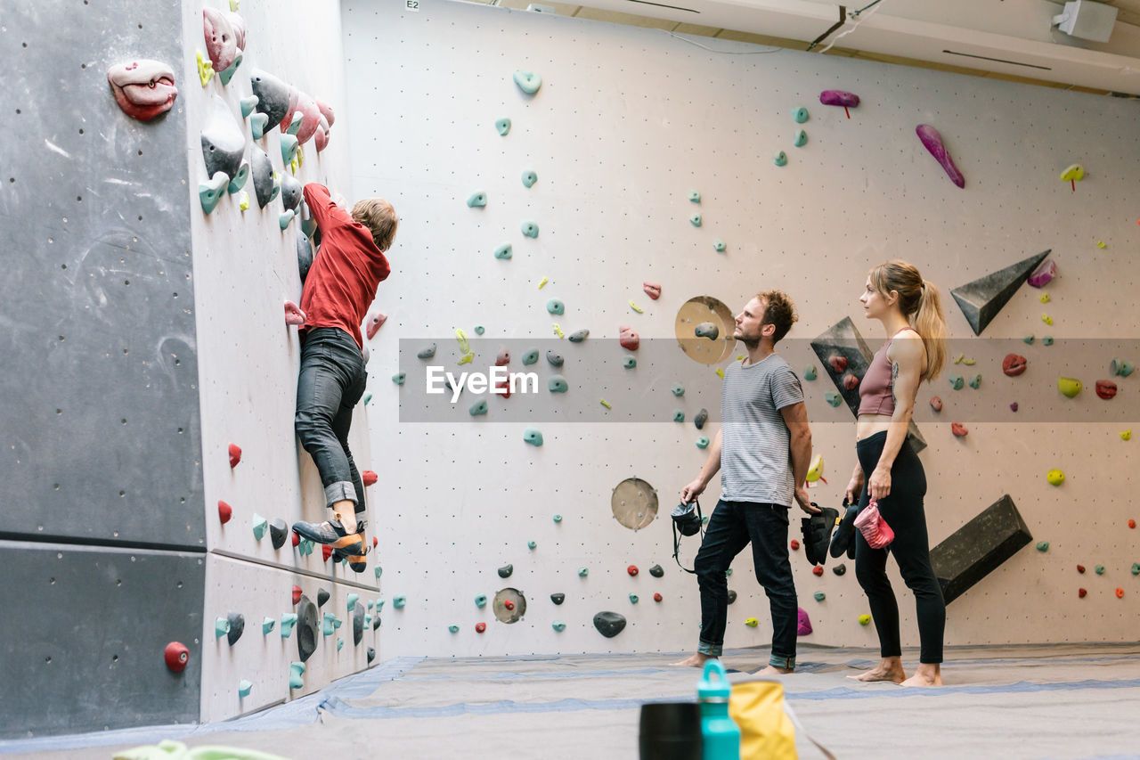 Side view of mature coach training male and female students for wall climbing in gym