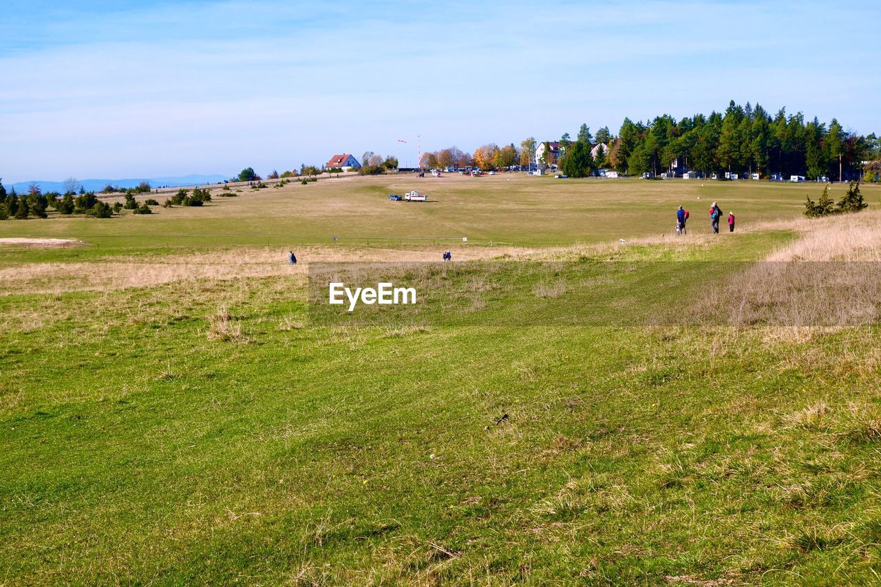 PEOPLE ON GREEN FIELD AGAINST SKY