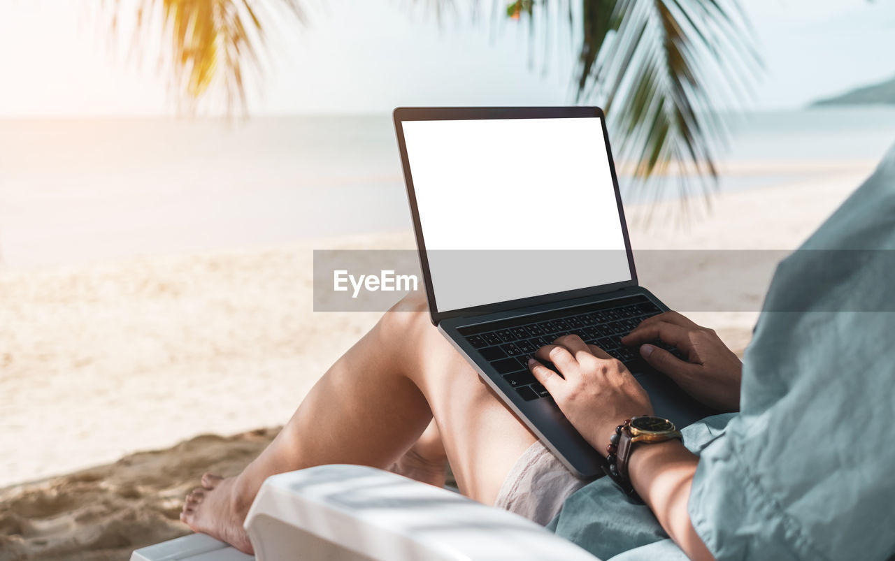 Midsection of woman using laptop at beach