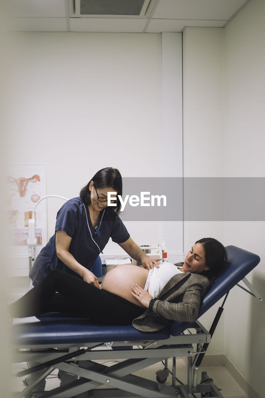 Smiling gynecologist measuring abdomen of pregnant woman lying on gurney in hospital