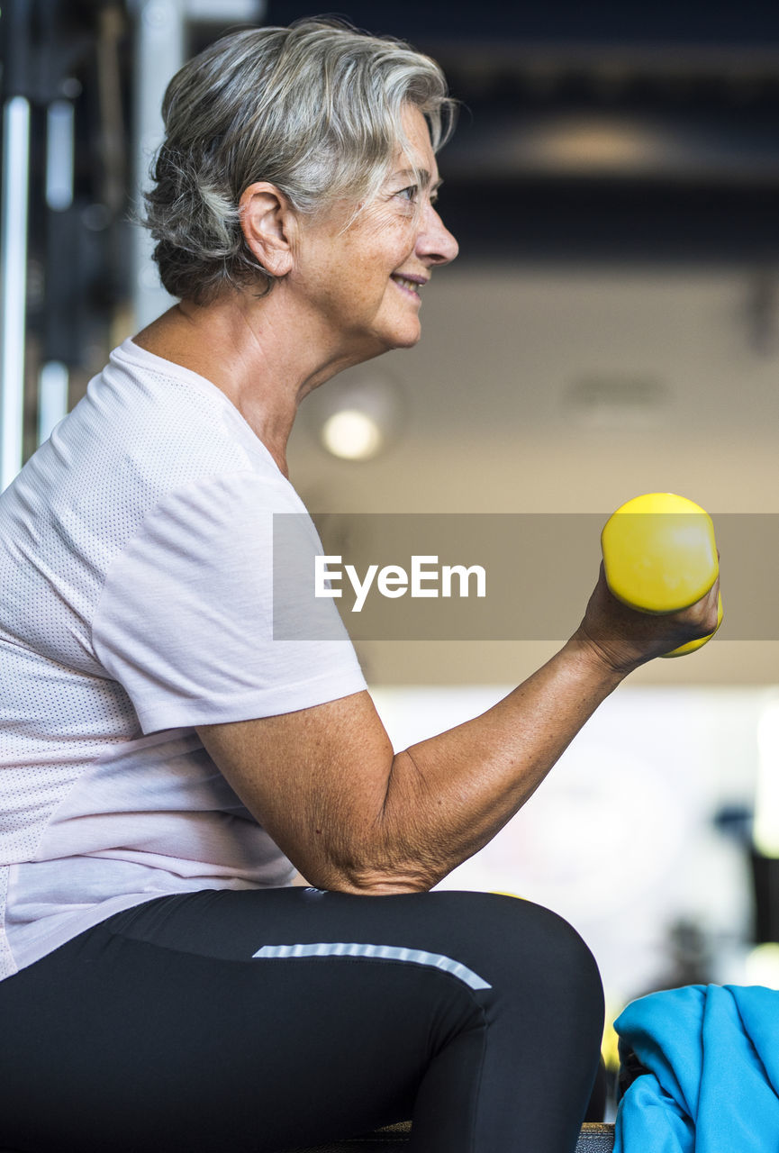 side view of young woman holding dumbbell at home