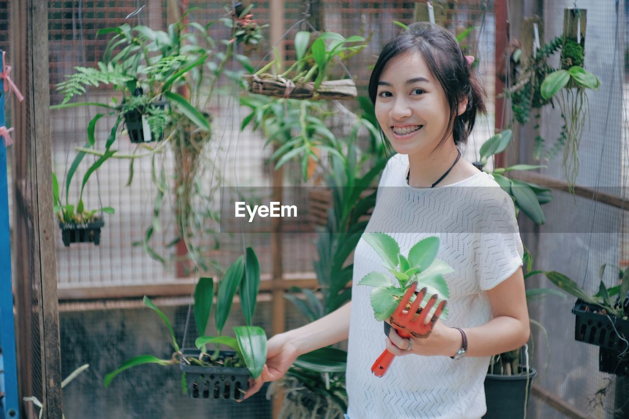 Portrait of young woman examining plants in greenhouse