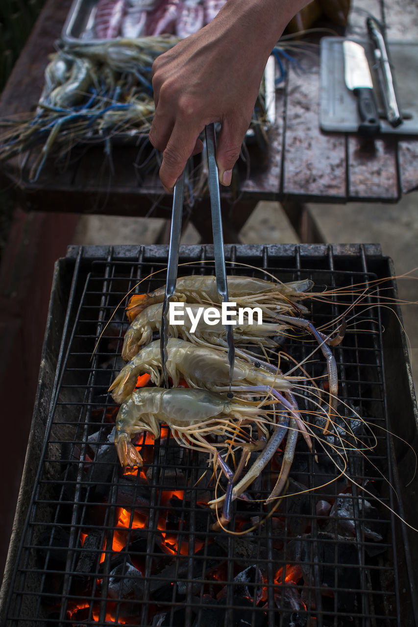 Cropped hand grilling crayfish on barbecue