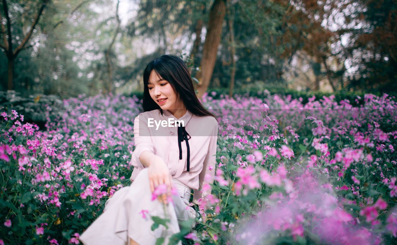 PORTRAIT OF A SMILING YOUNG WOMAN SITTING ON PINK CHERRY BLOSSOM