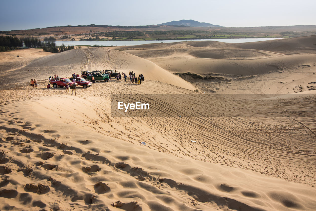 Group of people with vehicles on sand dune in desert