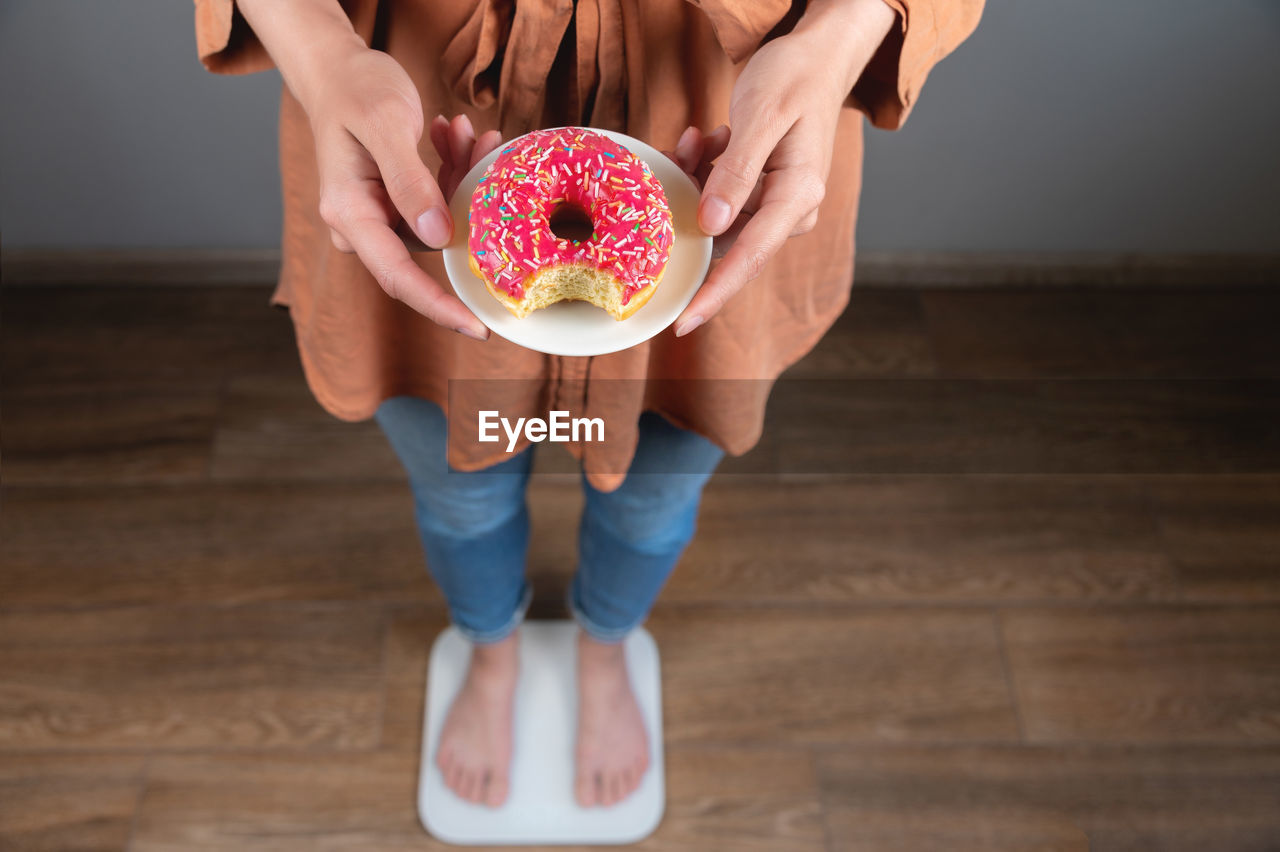 Diet. a woman measures body weight on a scale, holding a donut on a plate. sweets, unhealthy junk