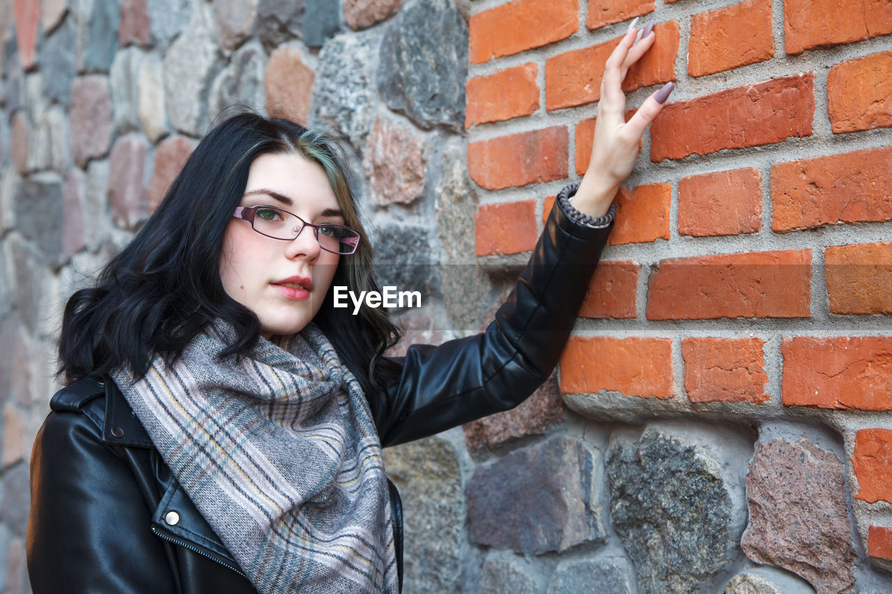 portrait of woman standing against brick wall