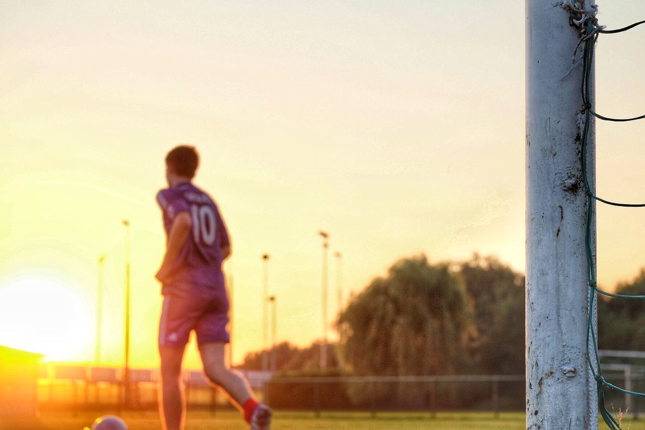 Rear view of man playing g soccer in field during sunset