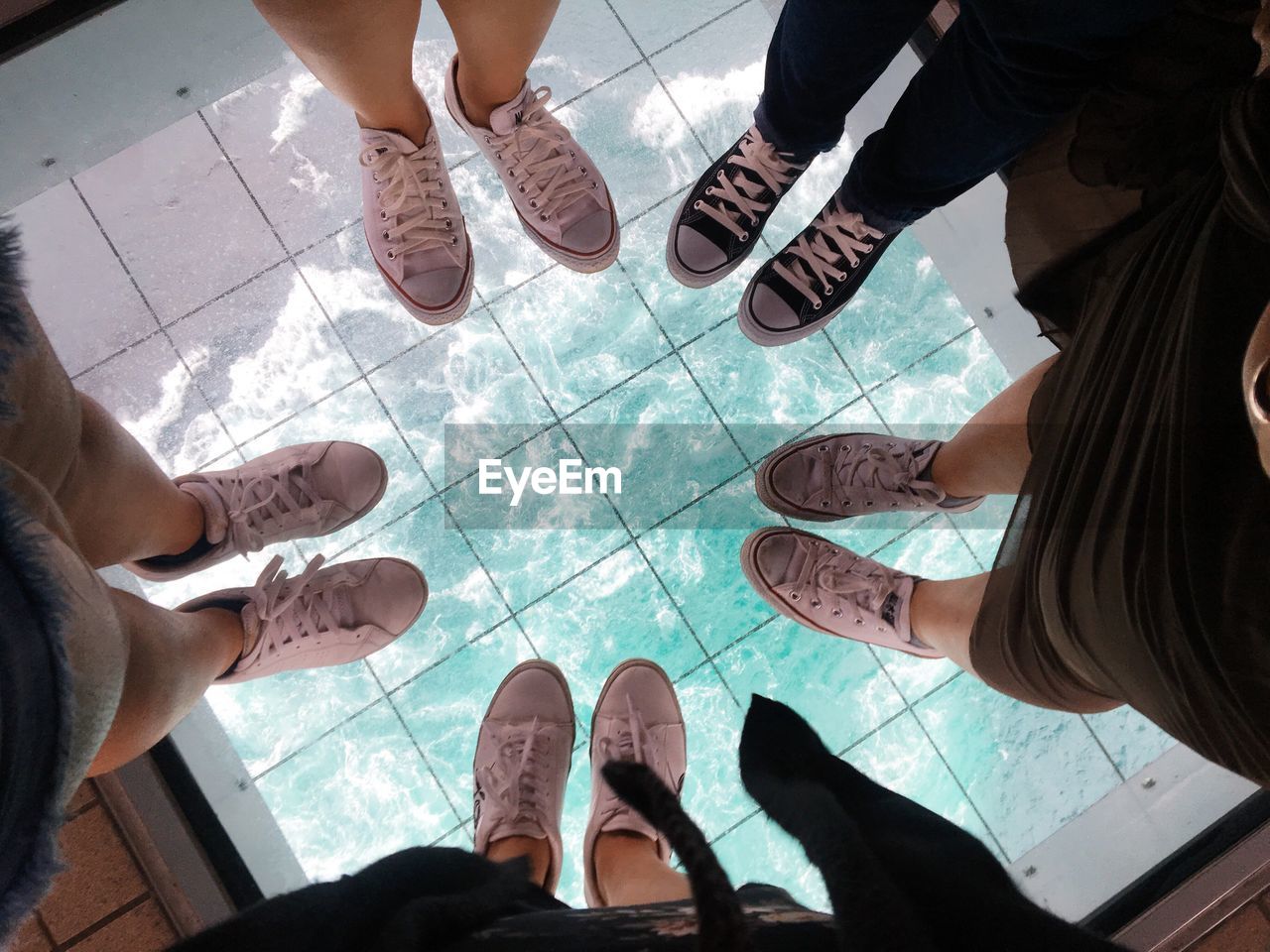 Low section of friends standing on glass floor 