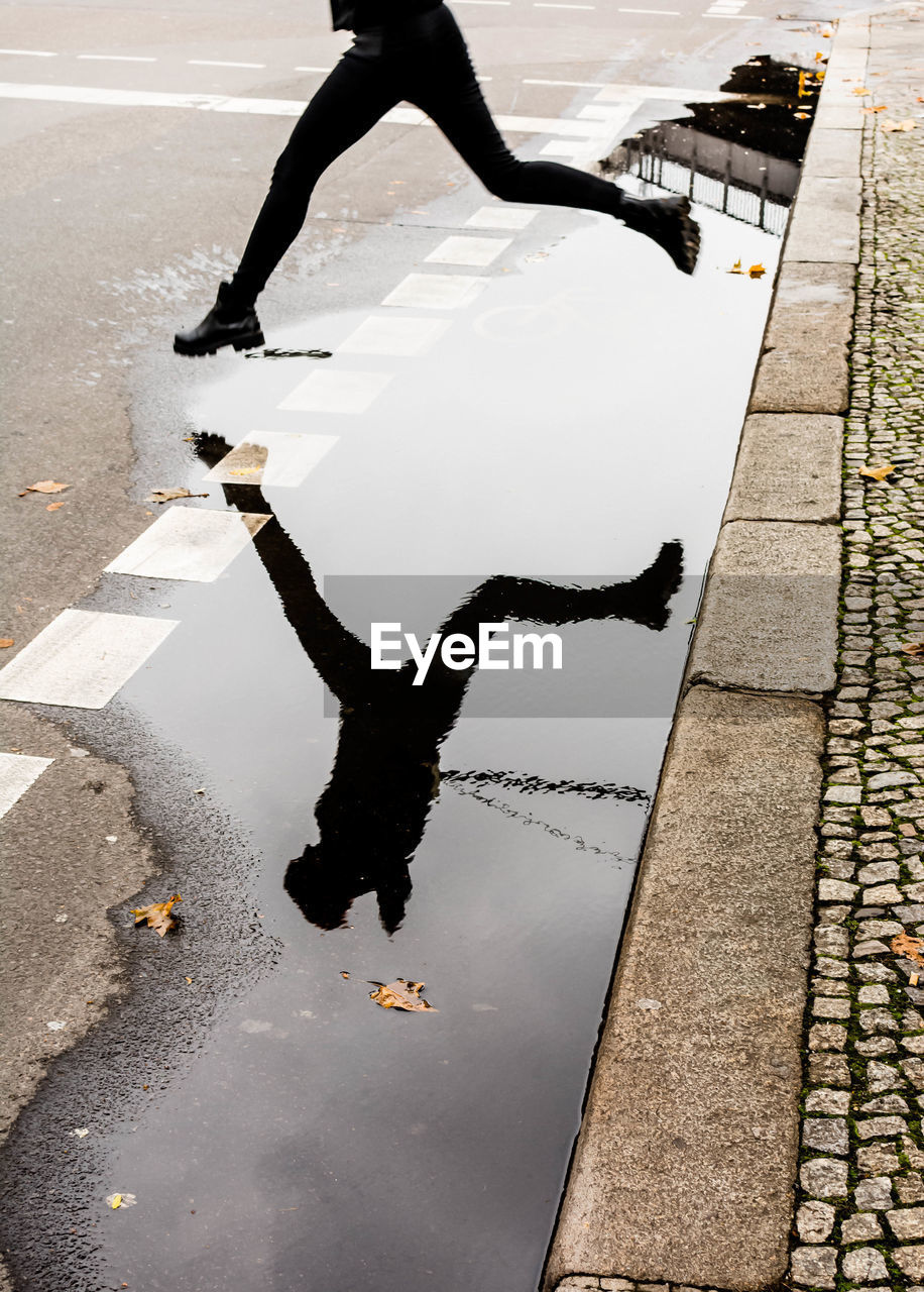 Low section of man jumping over puddle on street during rainy season