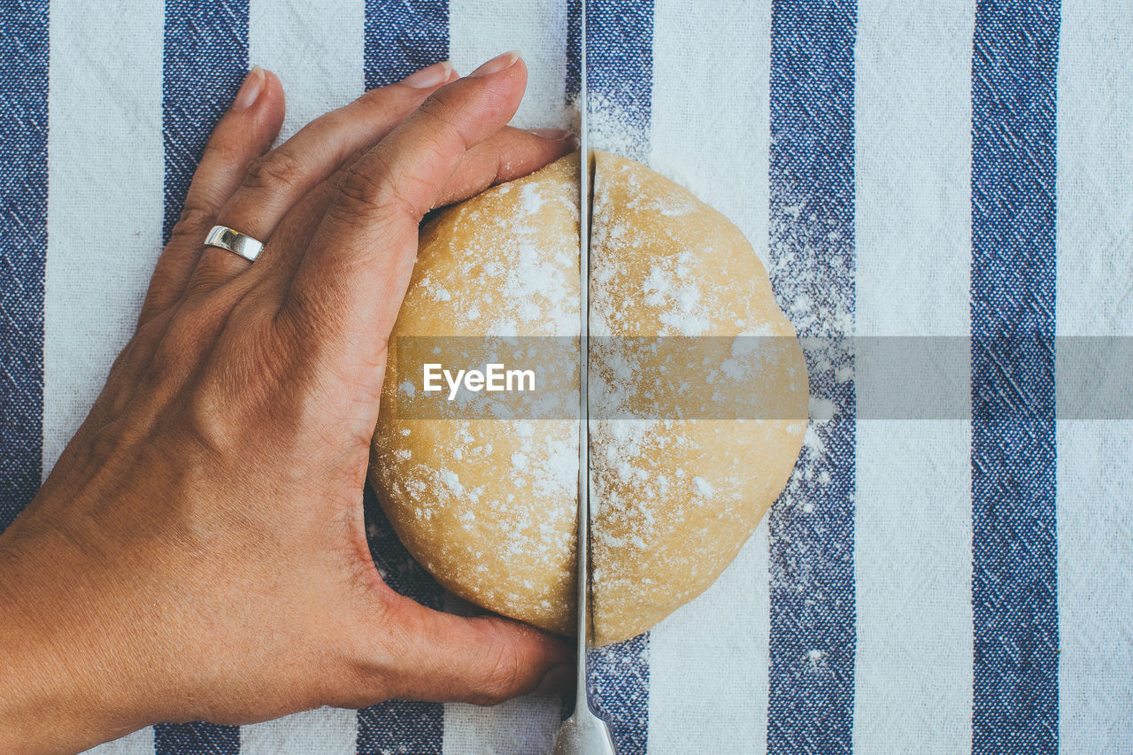 Cropped image of hand cutting bread on table at home